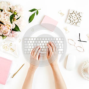 Flat lay women`s office desk. Female workspace with female hands, computer, pink peonies bouquet, accessories on white