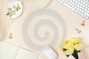 Flat lay women`s office desk. Female workspace with keyboard, bouquet of tulips, accessories, diary, glasses on a beige paper