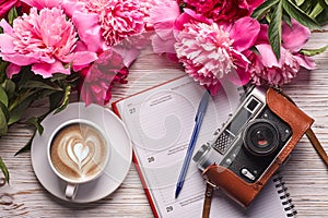 Flat lay women`s office desk. Female workspace with laptop, pink peonies bouquet, camera and coffee on white background.