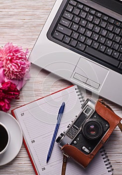 Flat lay women`s office desk. Female workspace with laptop, pink peonies bouquet, camera and coffee on white background