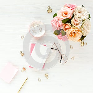 Flat lay women`s office desk. Female workspace with pink roses flowers bouquet, accessories, golden diary, glasses on