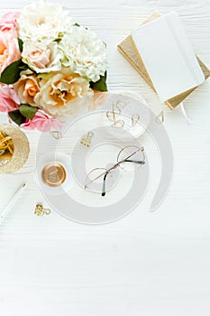 Flat lay women`s office desk Female workspace with pink roses flowers bouquet, accessories, golden diary, glasses on