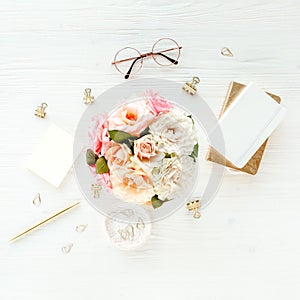 Flat lay women`s office desk Female workspace with pink roses flowers bouquet, accessories, golden diary, glasses on