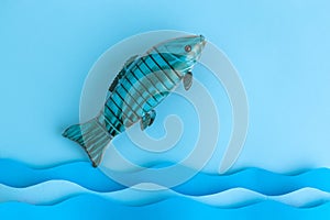 Flat lay of wooden fish with water made of paper abstract against pastel blue background