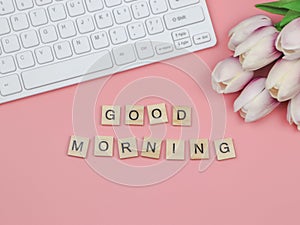 Flat lay of wooden letter on pink background with computer keyboard and tulip flower bouquet