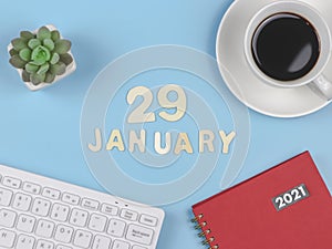 Flat lay of wooden letters 29 JANUARY on blue background with red 2021 diary, computer keyboard, cup of black coffee and