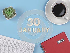 Flat lay of wooden letters 30 JANUARY on blue background with red 2021 diary, computer keyboard, cup of black coffee and