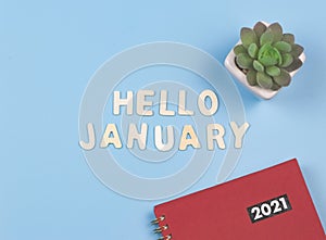 Flat lay of wooden letters HELLO JANUARY  with  red 2021 diary or planner and succulent plant pot on blue background . greeting