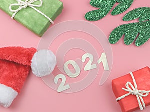 Flat lay of wooden number 2021 on pink background with Christmas hat, green reindeer horn and gift boxes. Happy new year 2021