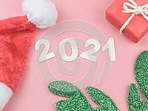 Flat lay of wooden number 2021 on pink background with Christmas hat, green reindeer horn and red gift box. Happy new year 2021