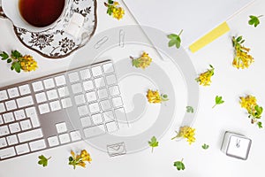 Flat lay of workplace with yellow barberry flowers, tea cup and keyboard