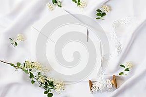 Flat lay workspace, mockup. Wedding invitation cards, craft envelopes,white flowers, green leaves and lace on white