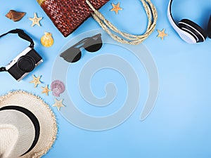 Flat lay of  woven or rattan bag, camera, straw hat, sunglasses and headphones  on blue background, decorated with sea shells and