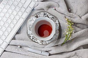 Flat layout of tea in silver mug with saucer, bird cherry flowers and keyboard