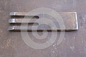 A flat rectangular piece of steel with three symmetrical tine tools lying on it, shown from above in a flat layout