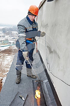 Flat roof installation. Workers melting bitumen roofing felt