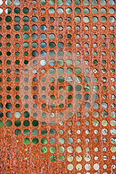 Flat sheet of iron with round holes in various sizes, pattern and texture in orange rust from extensive oxidation, as an abstract