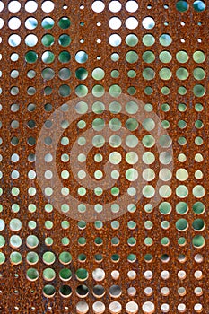 Flat sheet of iron with round holes in various sizes, pattern and texture in orange rust from extensive oxidation, as an abstract