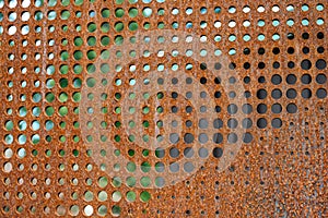 Flat sheet of iron with round holes in various sizes, pattern and texture in orange rust from extensive oxidation, as an abstract