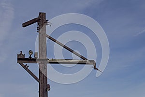 Flat steel poles with outriggers and light fixtures against blue sky, rusted metal patina