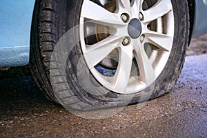 Flat tire of blue car on the road waiting for repair. Car tire leak because of nail pounding