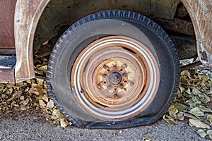 A flat tire on a rusty antique car