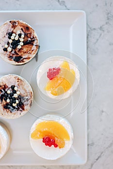 Flat view of beautiful cream cakes with berries and fruits on white ceramic plate.