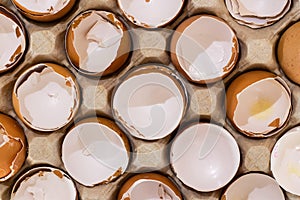 Flat view of a box with broken eggshell brown chicken eggs, background texture pattern