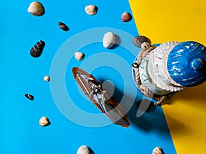 Flat view of toy sailboat and lighthouse on blue and yellow background with sea stones and seashells