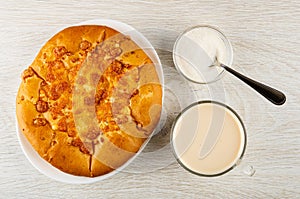 Flatbread with cheese in plate, spoon in bowl with sugar, cup with fermented baked milk on wooden table. Top view