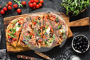 Flatbread pizza garnished with fresh arugula on wooden pizza board, top view