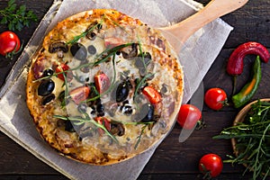 Flatbread pizza garnished with fresh arugula on wooden pizza board, top view. Dark stone background. Person picking slice of pizza