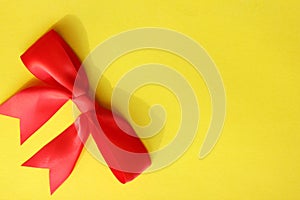 Flatlay beautiful red bright four-contour festive gift bow of satin ribbon on a yellow background. Holiday and packaging. View