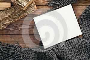 Flatlay book with empty page, grey knitted scarf, firewood on wooden background. Flat lay, top view, overhead. Cozy autumn home