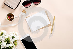 Flatlay composition with feminine accessories, blank paper card mockup, tea cup, smartphone, sunglasses, daisy flowers on pastel