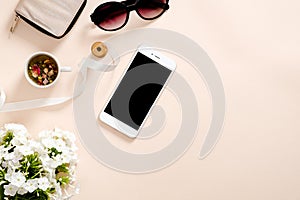 Flatlay composition with feminine accessories, tea cup, smartphone blank screen mockup, sunglasses, daisy flowers on pastel pink