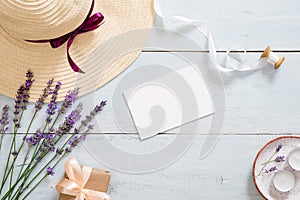 Flatlay composition with straw hat, lavender flowers, paper card mockup, ribbon, gift box, candle. Feminine desk table with