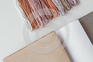 Flatlay creativity: canva aida beige, gray and white and multi-colored floss thread,