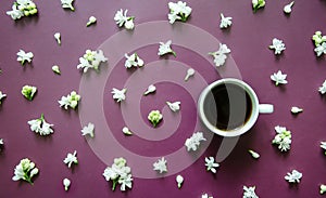 Flatlay dark purple background with small white lilac flowers, white coffee cup on textured background