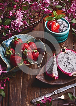 Flatlay food background - empty wooden board with dragon fruit, strawberries and pink flowers, copy space