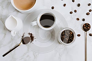 Flatlay of fresh cups of espresso and milk coffee, creamer, coffee beans and spoon on marble background