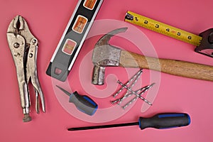 Flatlay of Hand Tools on Pink Background Including Hammer, Nails, Tape Measure, Level, Screwdrivers