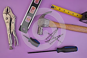 Flatlay of Hand Tools Purple Background Including Hammer, Nails, Tape Measure, Level, Screwdrivers