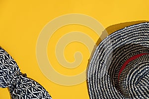 Flatlay hat and swimsuit in blue and white stripes are a bright yellow background. Concept of summer vacation at sea.