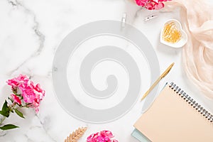 Flatlay home office desk table. Workspace with pale pastel beige notebook, pink flowers and decorations on white background. Flat