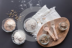 Flatlay of ingredients to bake homemade sourdough: rye, wholegrain, plain wheat flour, seeds, starter, salt, yeast