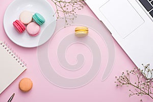Flatlay of laptop, cake macaron and cup of tea on pink table. Be