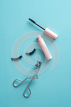 Flatlay mascara, false eyelashes, eyelash curler on blue background. Makeup cosmetics set top view