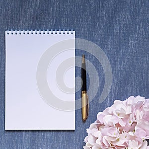 Flatlay with mockup. Notepad clean with a blank page for writing text, pen, pink hydrangea flowers on a blue background