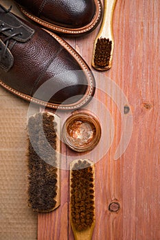 Flatlay of Various Shoes Cleaning Accessories for Dark Brown Grain Brogue Derby Boots Made of Calf Leather Over Paper Background